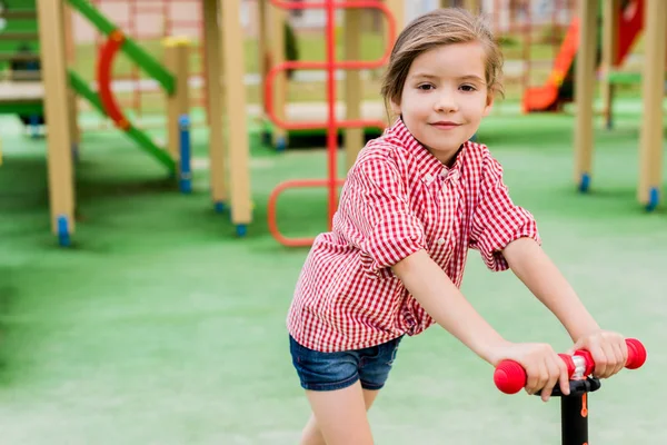 Foco seletivo de criança pequena montando em scooter pontapé no parque infantil — Fotografia de Stock