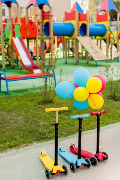 Tres pateadores infantiles colocados en fila con globos de aire de colores en el patio de recreo - foto de stock