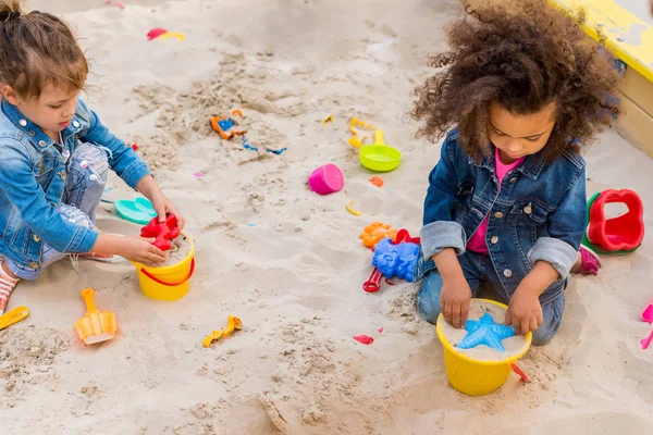 Visão de alto ângulo de duas crianças multiculturais usando moldes de plástico em sandbox no parque infantil — Fotografia de Stock