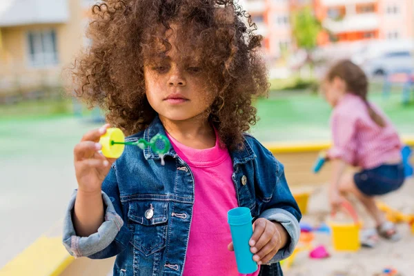 Enfoque selectivo de rizado afroamericano niño pequeño jugando con soplador de burbujas - foto de stock