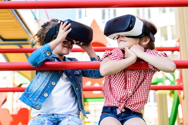 Селективный взгляд на двух маленьких детей с помощью наушников виртуальной реальности на детской площадке — стоковое фото