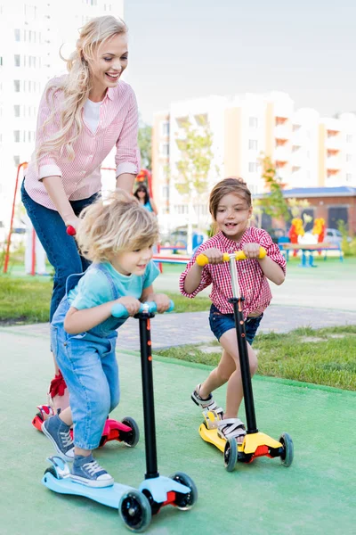 Selective focus of mother riding on kick scooters with son and daughter at playground — Stock Photo