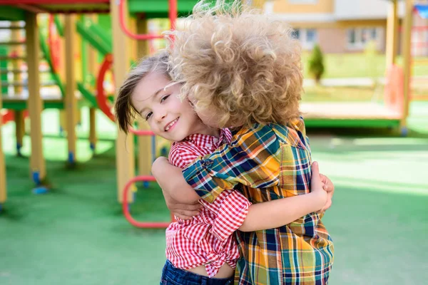 Selective focus of curly boy kissing and hugging little sister at playground — Stock Photo