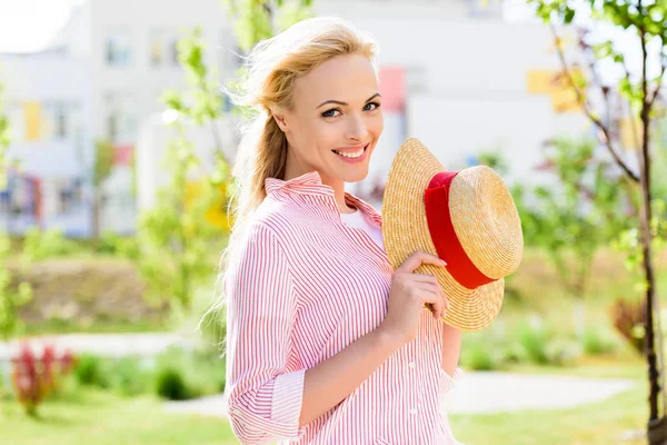 Portrait of smiling young woman in straw hat on blurred background — Stock Photo