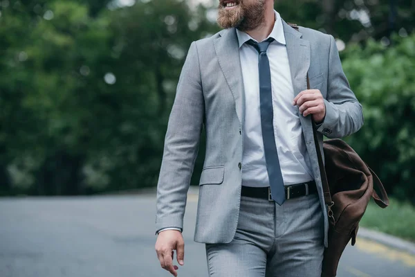 Imagen recortada de un hombre de negocios sonriente caminando por la calle en traje gris - foto de stock