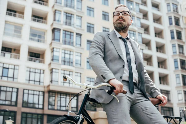 Handsome businessman in suit leaning on bicycle in city — Stock Photo