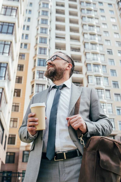 Vista inferior del hombre de negocios en traje con bolsa de cuero sosteniendo café para llevar - foto de stock