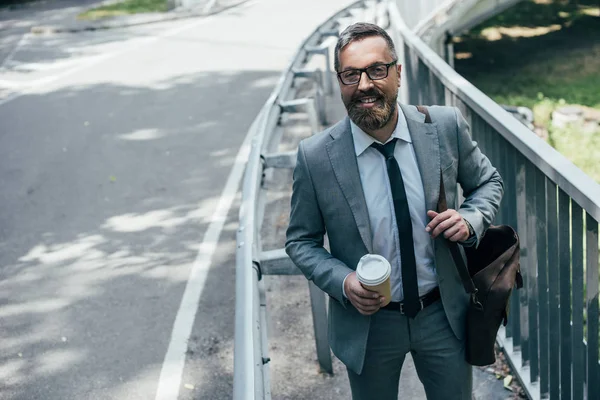 Homem de negócios em terno com saco de couro e café para ir andando na cidade — Fotografia de Stock