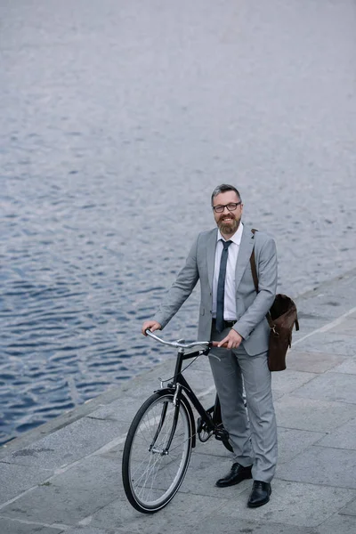 Homem de negócios bonito com saco de couro em pé no cais com bicicleta — Stock Photo