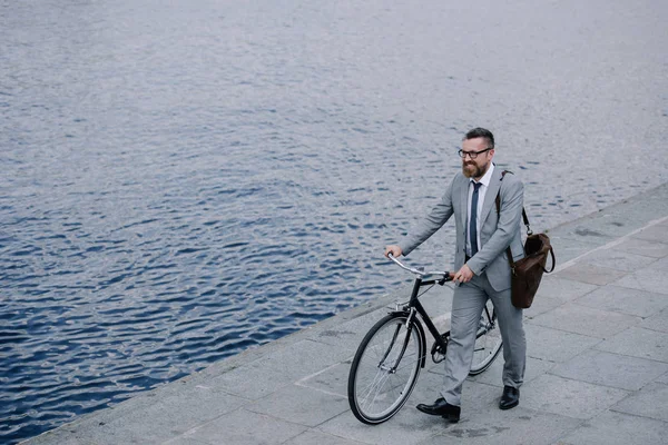 Homem de negócios bonito em terno andando com bicicleta no cais — Stock Photo