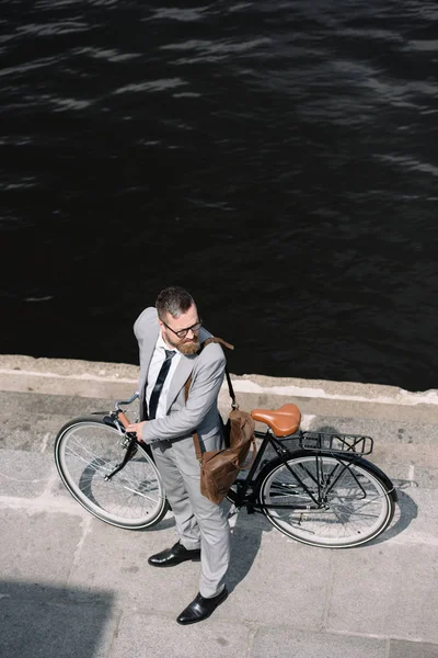 Vista aérea do empresário barbudo com bicicleta em pé no cais perto do rio — Fotografia de Stock