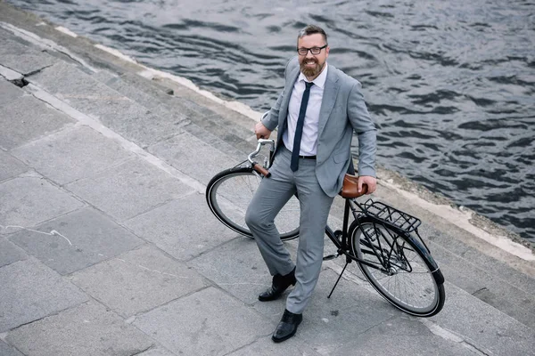 Вид сверху на бизнесмена, стоящего с велосипедом на набережной возле реки — стоковое фото