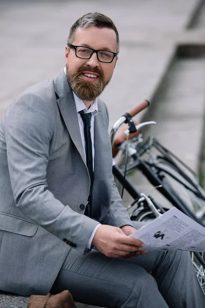 Bonito barbudo empresário com jornal sentado em escadas com bicicleta — Fotografia de Stock
