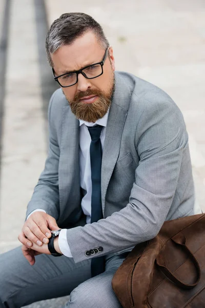 Красивый бородатый бизнесмен в сером костюме с кожаной сумкой и часами — стоковое фото