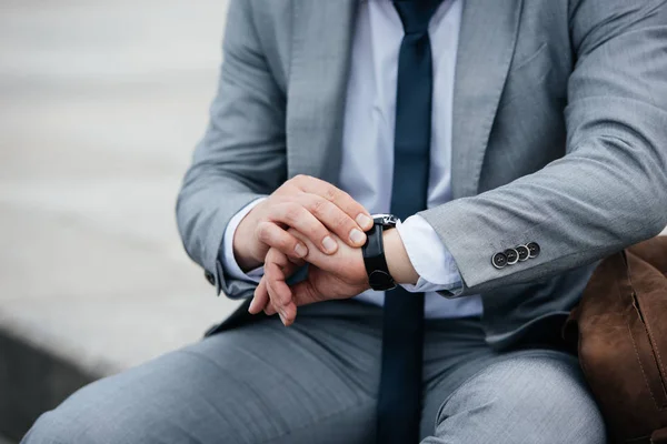 Vista ritagliata di uomo d'affari in abito grigio guardando orologio da polso — Foto stock