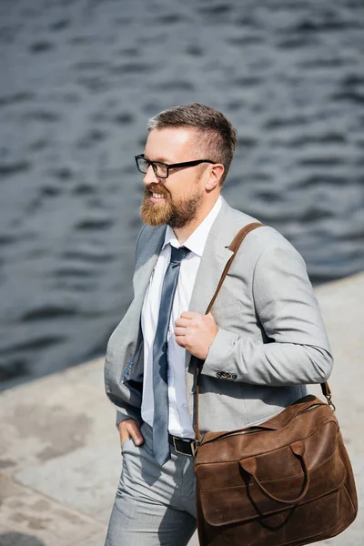 Bell'uomo d'affari barbuto in abito grigio con borsa in pelle che cammina sul molo — Foto stock