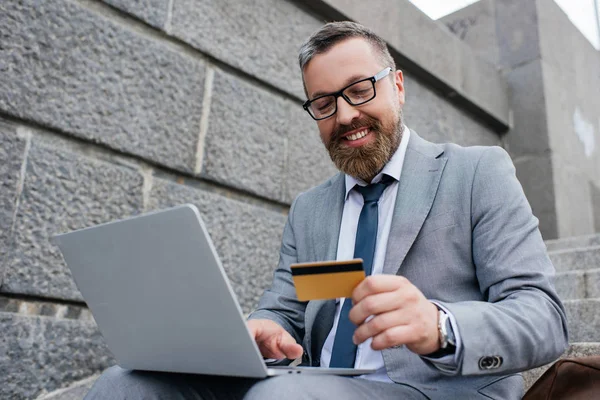 Homme souriant faisant des achats en ligne avec ordinateur portable et carte de crédit — Photo de stock