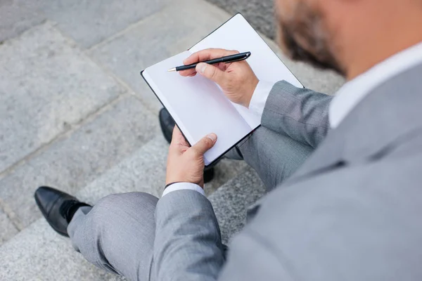 Cropped view of businessman in grey jacket writing in diary — Stock Photo