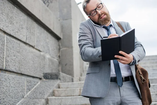 Homme d'affaires barbu avec sac en cuir écriture dans le planificateur — Photo de stock