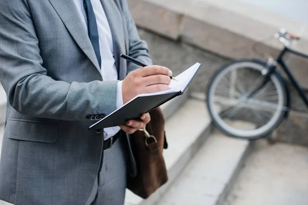 Cropped view of businessman with leather bag writing in diary — Stock Photo