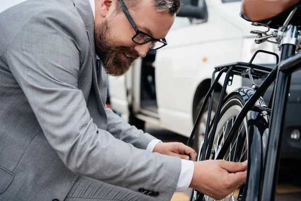 Homem de negócios barbudo em terno reparando roda de bicicleta — Stock Photo