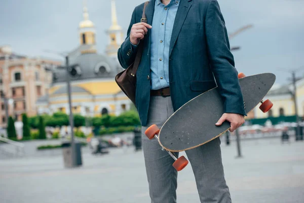 Vista recortada del hombre con bolsa de cuero y longboard caminar en la ciudad - foto de stock