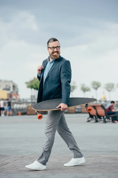 Hombre barbudo guapo con longboard caminando en la ciudad - foto de stock