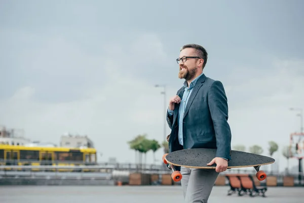 Stylish bearded man with skate walking in city — Stock Photo