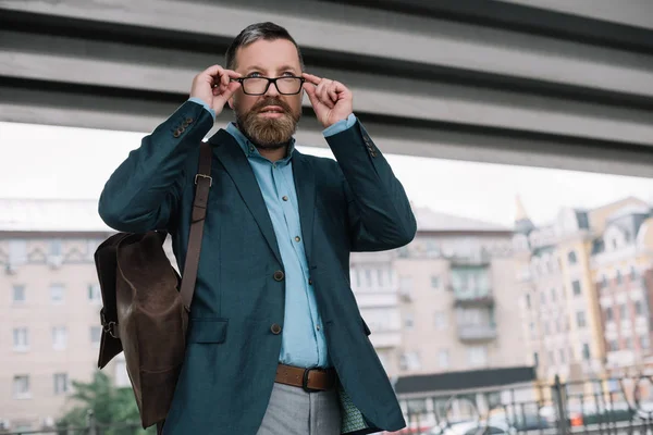 Beard stylish businessman in glasses with leather bag in city — Stock Photo