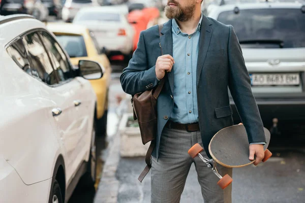 Cropped view of man with leather bag and longboard walking in city with cars — Stock Photo