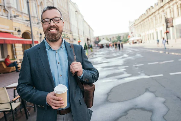 Стильный мужчина с кожаной сумкой и кофе, чтобы пойти гулять по городу — стоковое фото