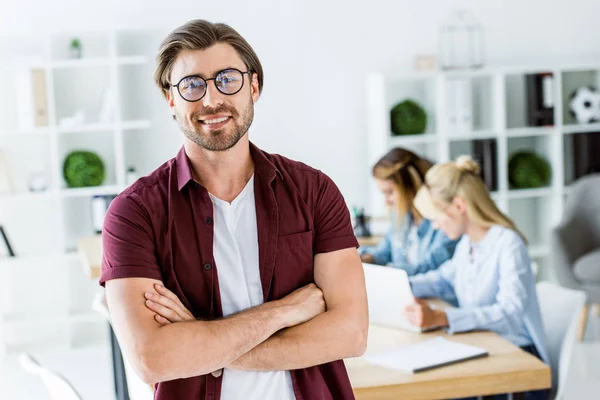 Schöner Mann steht mit verschränkten Armen im Büro eines Startup-Projekts und blickt in die Kamera — Stockfoto