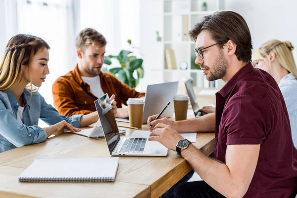 Colegas multiculturales que trabajan en el proyecto de puesta en marcha en la oficina con ordenadores portátiles y café - foto de stock