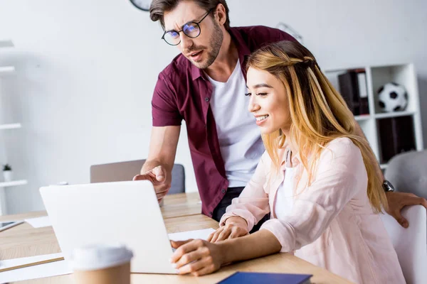 Colegas multiculturais trabalhando no projeto de startup no escritório e olhando para laptop — Fotografia de Stock