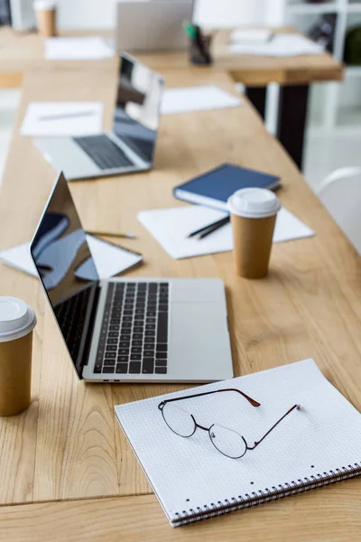 Ordinateurs portables avec tasses à café jetables sur la table dans le bureau d'affaires — Photo de stock