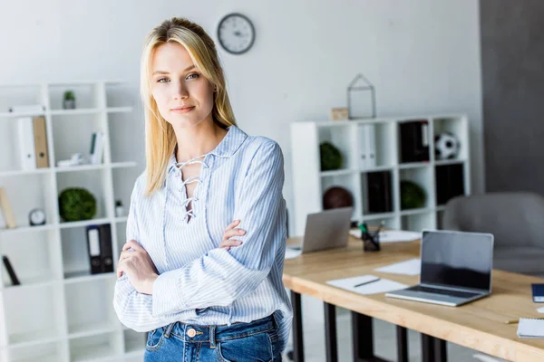 Beautiful businesswoman standing with crossed arms in office — Stock Photo