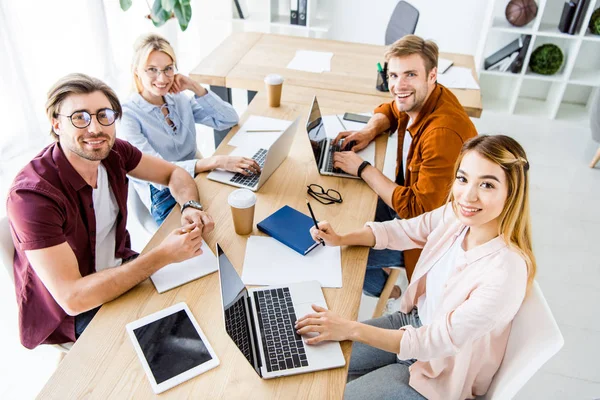 High angle view of multicultural colleagues working on startup project in office with gadgets and looking at camera — Stock Photo