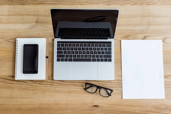Підвищений вид на ноутбук, смартфон і блокнот на столі у бізнес-офісі — стокове фото