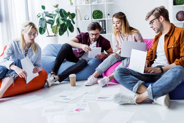 Colleghi multietnici che lavorano a un progetto di startup sul posto di lavoro con computer portatili e documenti — Foto stock