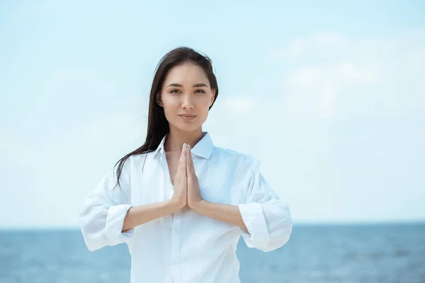 Focused asian woman doing namaste mudra gesture in front of sea — Stock Photo