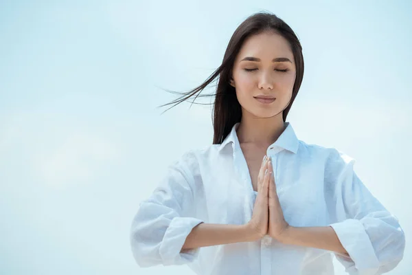 Азіатська жінка з закритими очима робить жест імаста мудра на блакитне небо — стокове фото