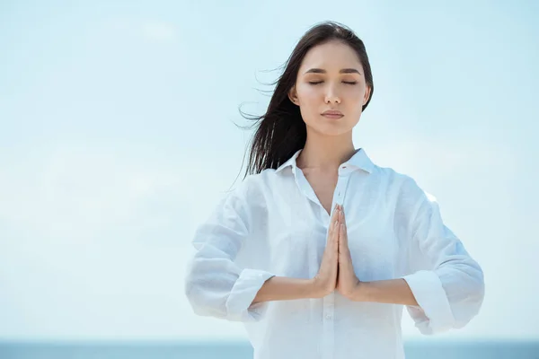 Concentrada mulher asiática com olhos fechados fazendo namaste mudra gesto na frente do mar — Fotografia de Stock