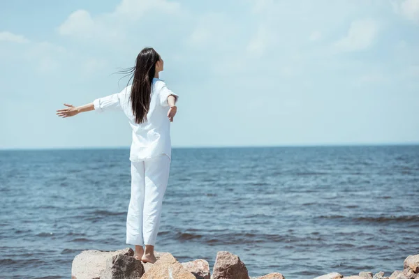 Rear view of young woman enjoying sea with arms outstretched on beach — Stock Photo