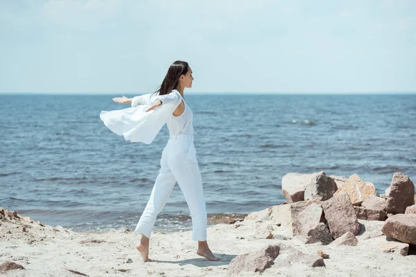 Vista lateral de mujer joven asiática disfrutando del mar con los brazos extendidos en la playa - foto de stock