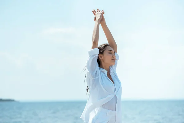 Attractive asian woman with closed eyes standing with wide arms in front of sea — Stock Photo