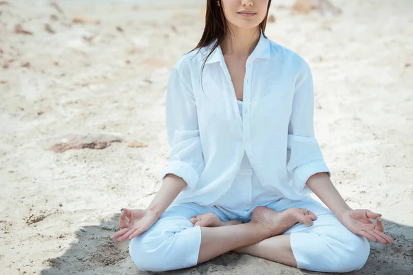 Imagen recortada de la mujer en ardha padmasana (media pose de loto) en la playa por mar - foto de stock