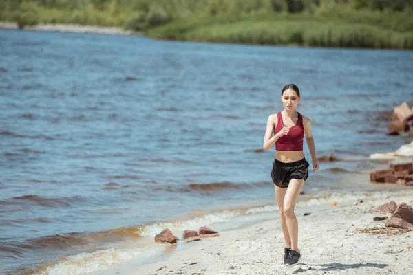 Front view of young asian female jogger running on beach — Stock Photo