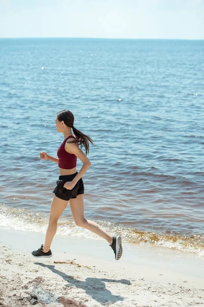 Side view of young asian sportswoman running on beach — Stock Photo