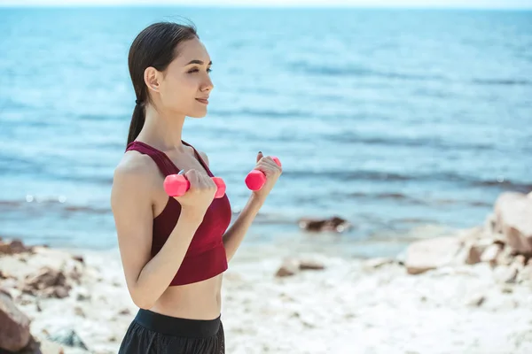 Side view of asian sportswoman exercising with dumbbells on beach — Stock Photo