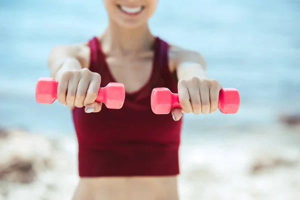 Imagen recortada de deportista sonriente haciendo ejercicio con pesas frente al mar - foto de stock